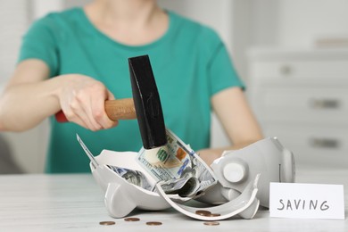 Photo of Financial savings. Woman breaking piggy bank with hammer at table indoors, closeup
