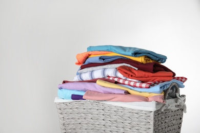 Wicker laundry basket with clean clothes on light background, closeup. Space for text