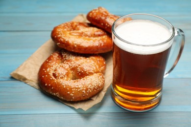 Mug of beer with tasty freshly baked pretzels on light blue wooden table, closeup