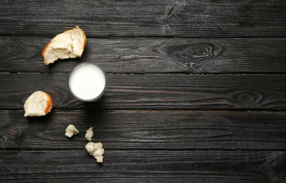 Glass of milk and bun pieces on wooden background, top view