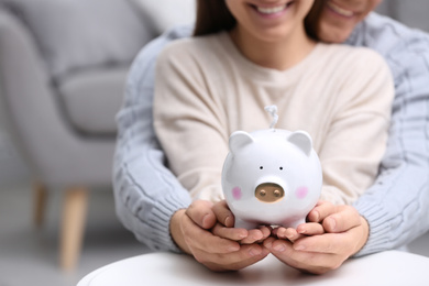 Photo of Couple with piggy bank at white table, closeup