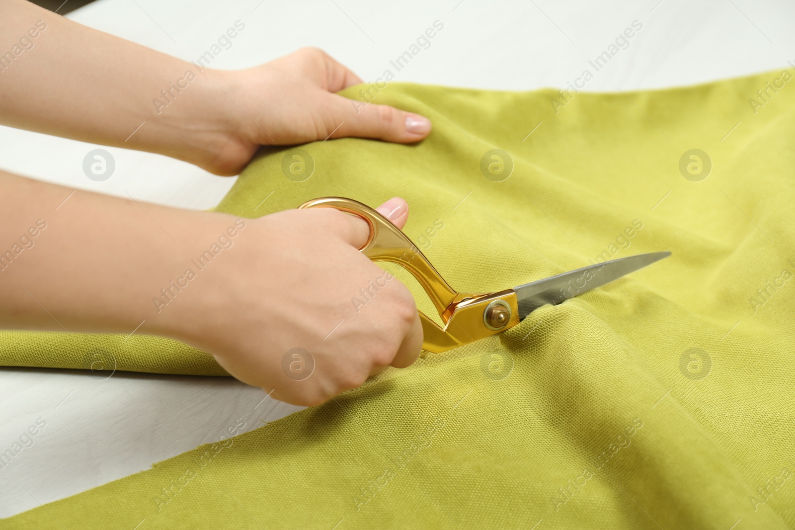 Photo of Seamstress cutting light green fabric with scissors at workplace, closeup