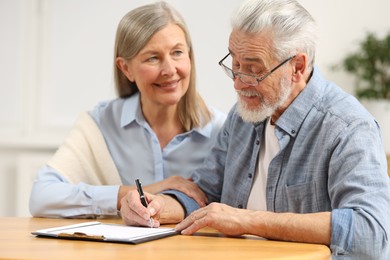 Happy senior couple signing Last Will and Testament indoors