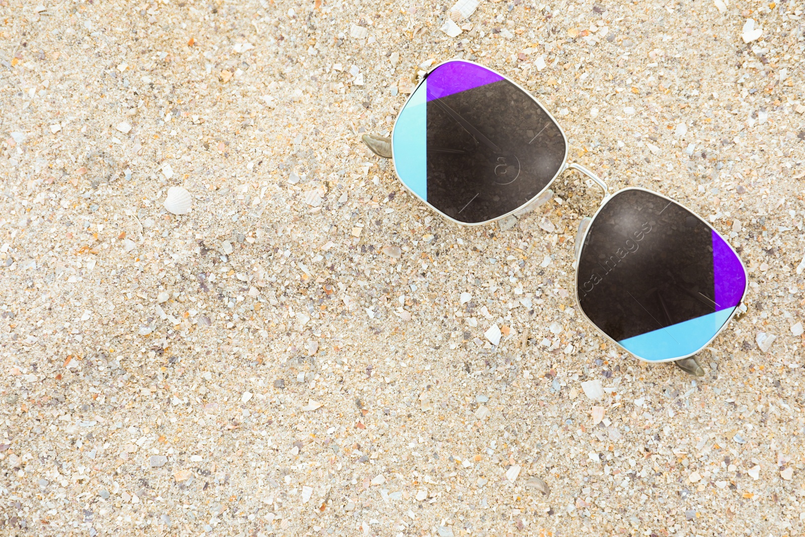 Photo of Stylish sunglasses on sandy beach, top view. Space for text