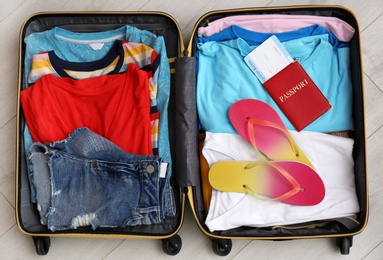 Packed suitcase with summer clothes and passport on wooden background, top view