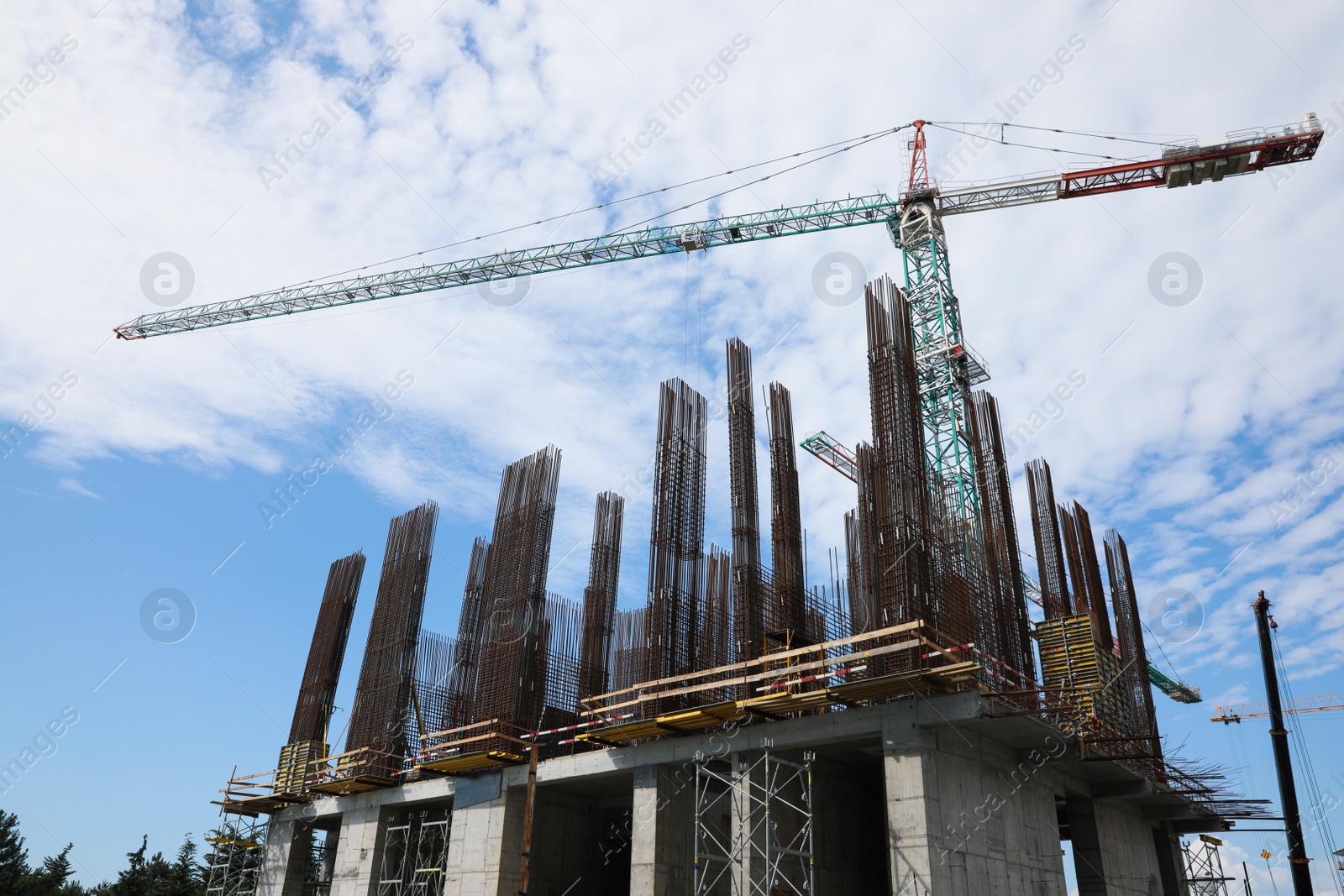 Photo of Tower crane near building under construction against cloudy sky