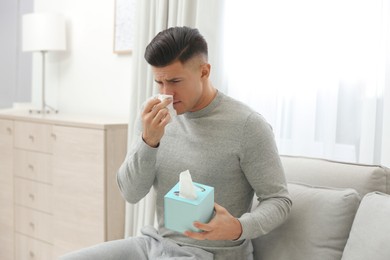 Photo of Ill man with box of paper tissues on sofa at home