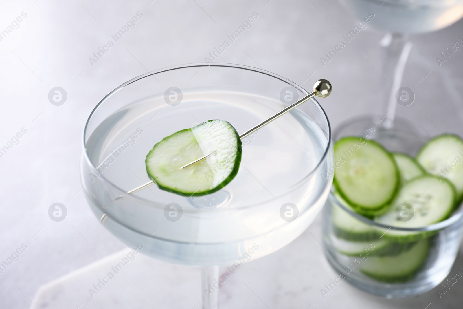 Photo of Glass of martini with cucumber on light table, closeup