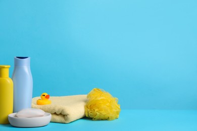 Photo of Baby cosmetic products, bath duck, sponge and towel on light blue background. Space for text