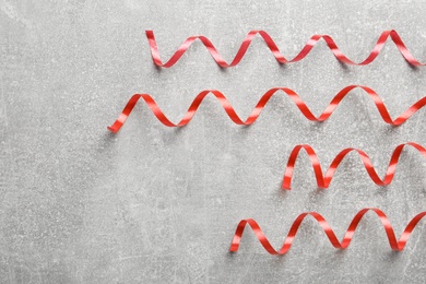 Photo of Shiny red serpentine streamers on grey background, flat lay. Space for text