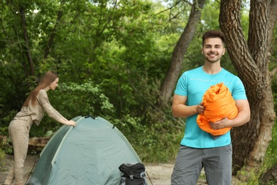 Image of Young man with sleeping bag and his girlfriend near camping tent in forest