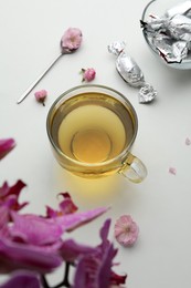 Glass cup of freshly brewed tea and flowers on light table