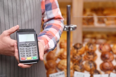 Photo of Cashier holding payment terminal in bakery, closeup. Space for text