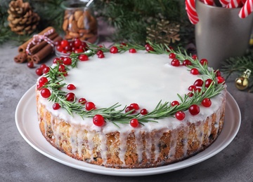 Traditional Christmas cake decorated with rosemary and cranberries on light grey table