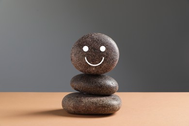 Stack of stones with drawn happy face on beige table against grey background. Zen concept