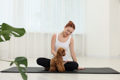 Happy young woman practicing yoga on mat with her cute dog indoors