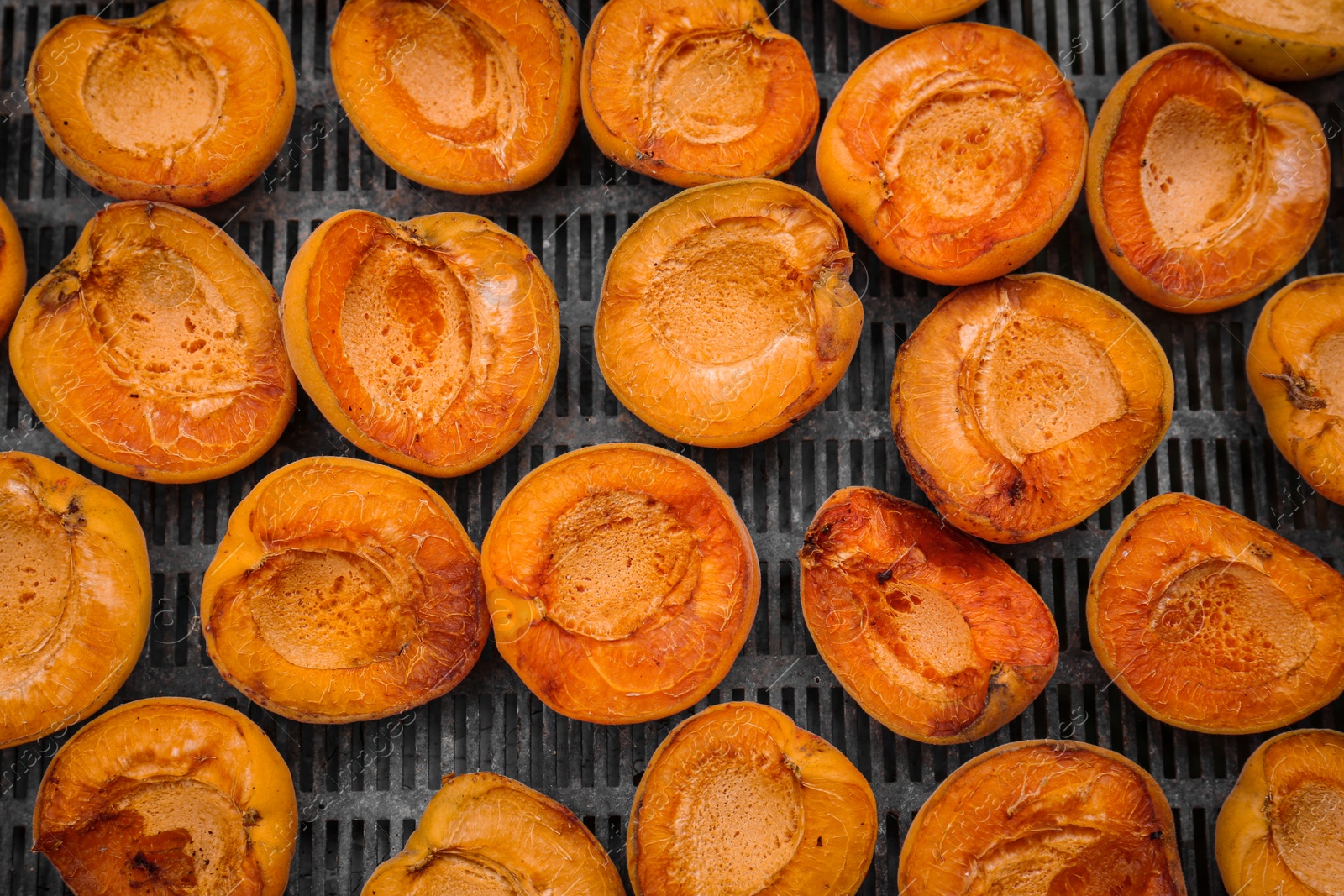 Photo of Many halved apricots on metal drying rack, flat lay