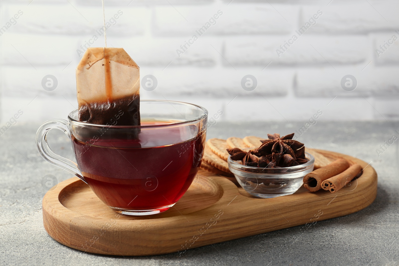 Photo of Tea bag in glass cup, anise stars and cinnamon sticks on light grey table