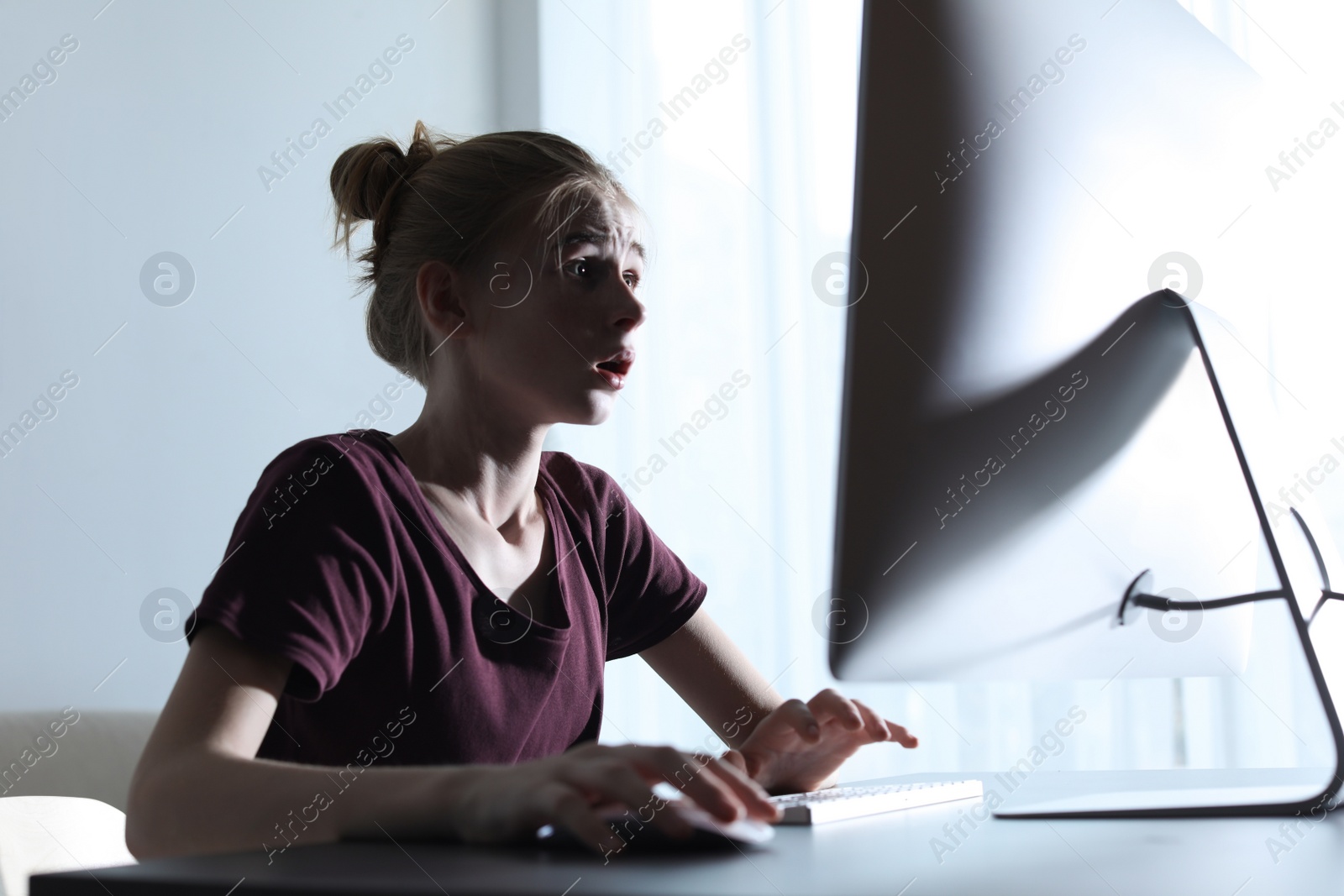 Photo of Shocked teenage girl using computer at table indoors. Danger of internet