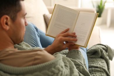 Photo of Man covered with warm green plaid reading book at home, closeup