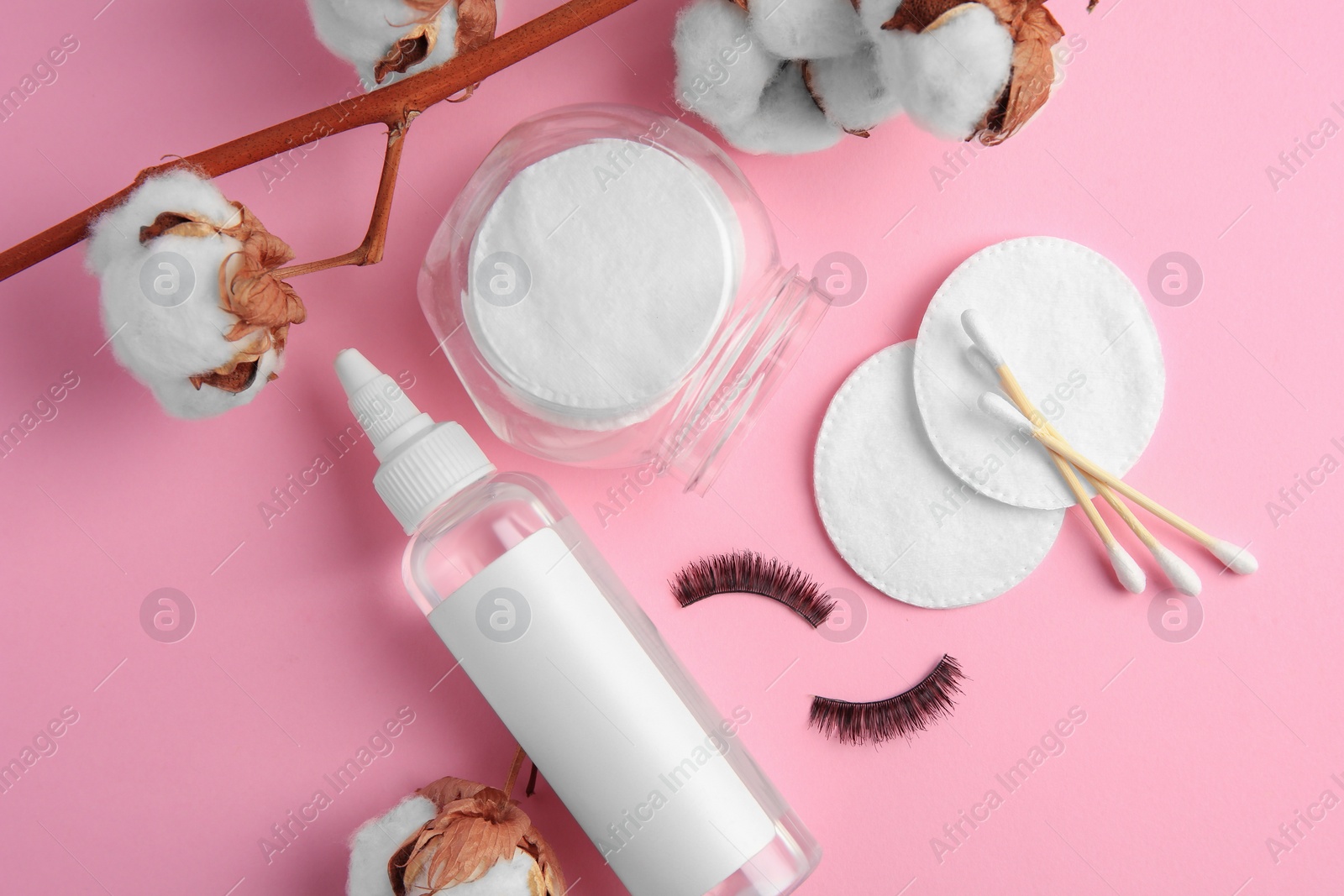 Photo of Bottle of makeup remover, cotton flowers, pads, swabs and false eyelashes on pink background, flat lay