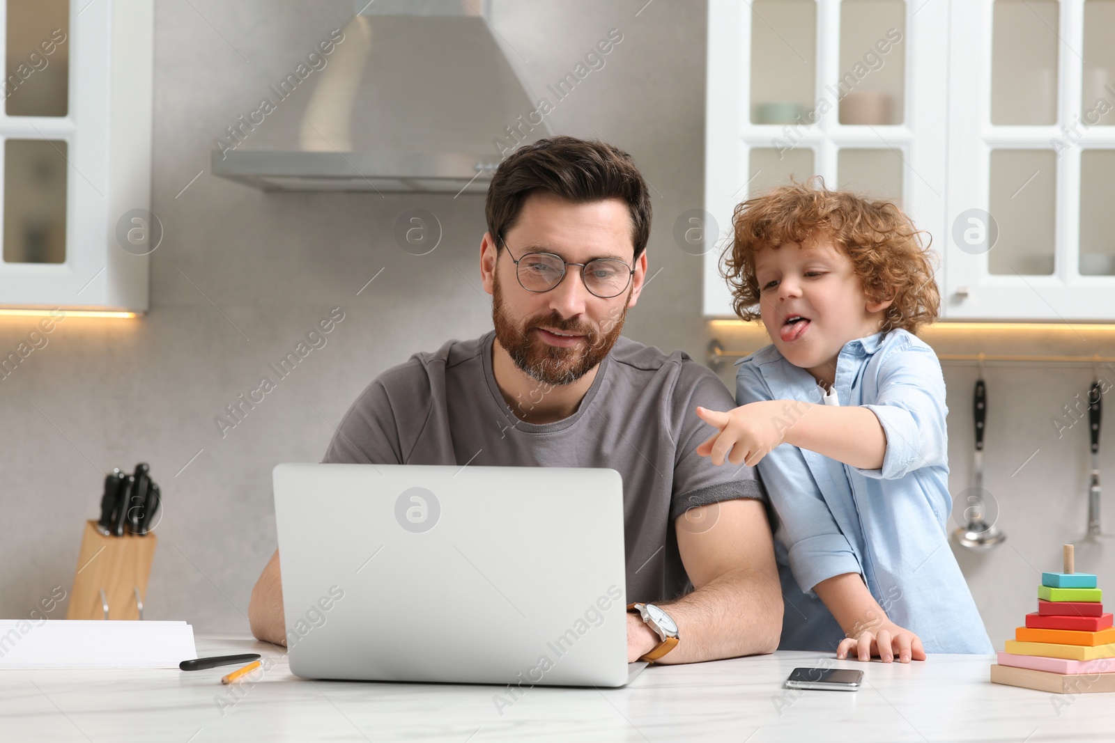 Photo of Man with laptop working remotely at home. Father and son at desk