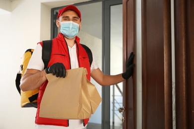 Courier in protective mask and gloves with order at entrance. Restaurant delivery service during coronavirus quarantine