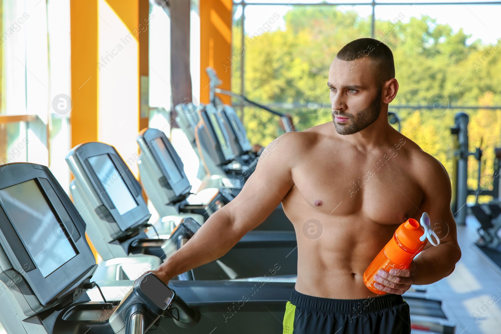 Photo of Portrait of athletic man with protein shake on treadmill in gym