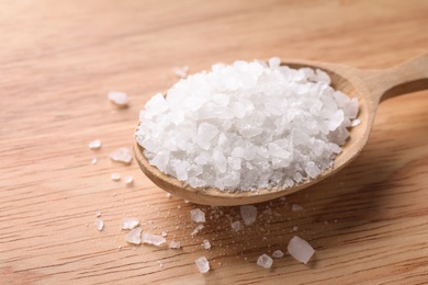 Photo of Spoon with white sea salt on wooden table, closeup. Spa treatment