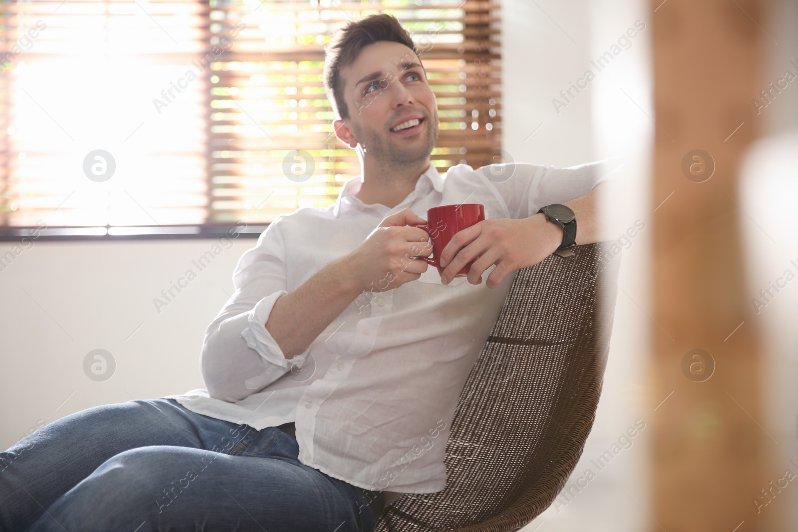 Photo of Young man with cup of drink relaxing near window at home