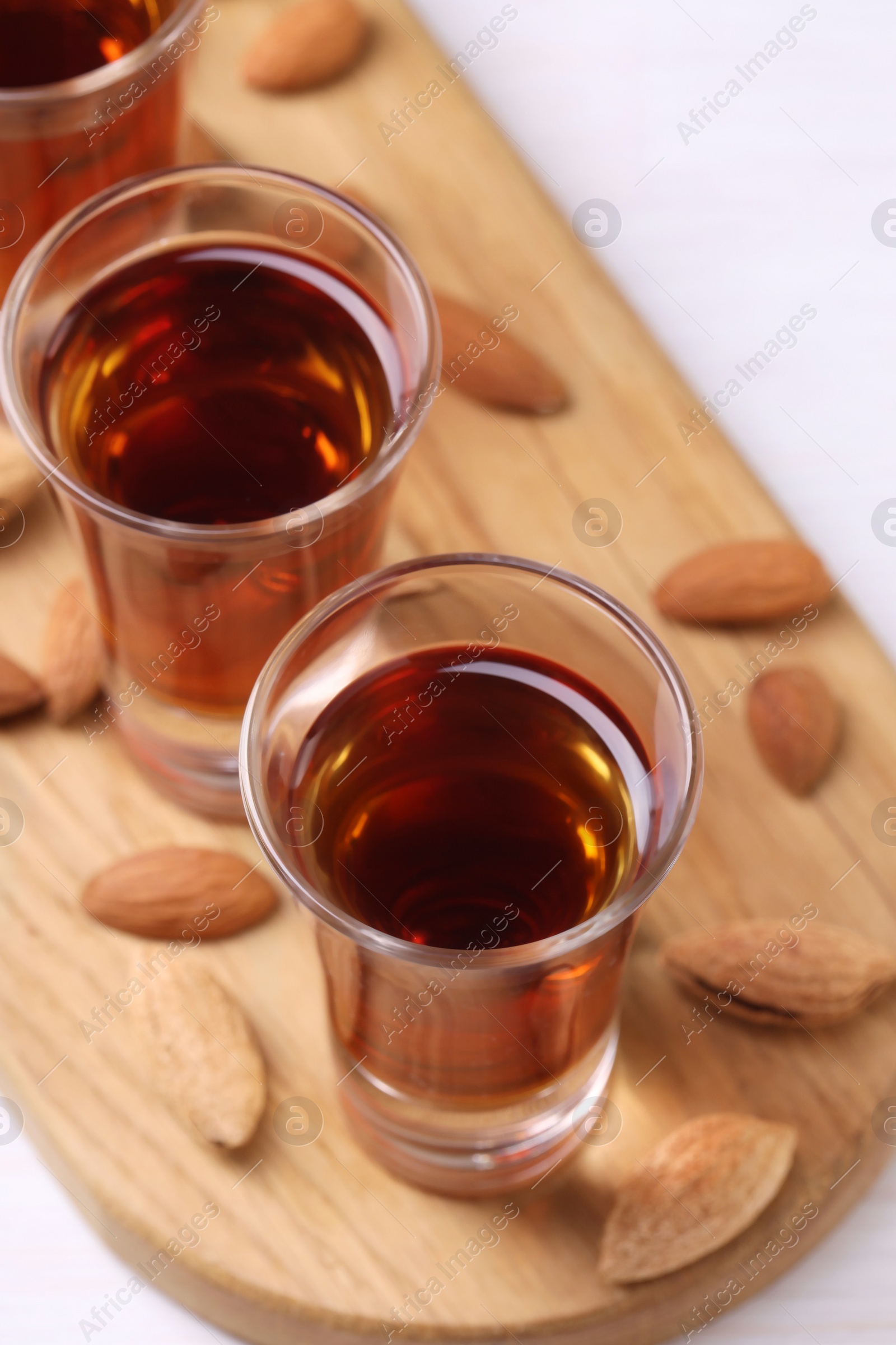 Photo of Shot glasses with tasty amaretto liqueur and almonds on white wooden table, closeup