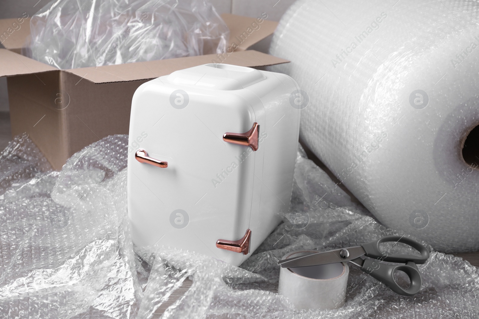 Photo of Cosmetics refrigerator with bubble wrap, scissors and adhesive tape on table