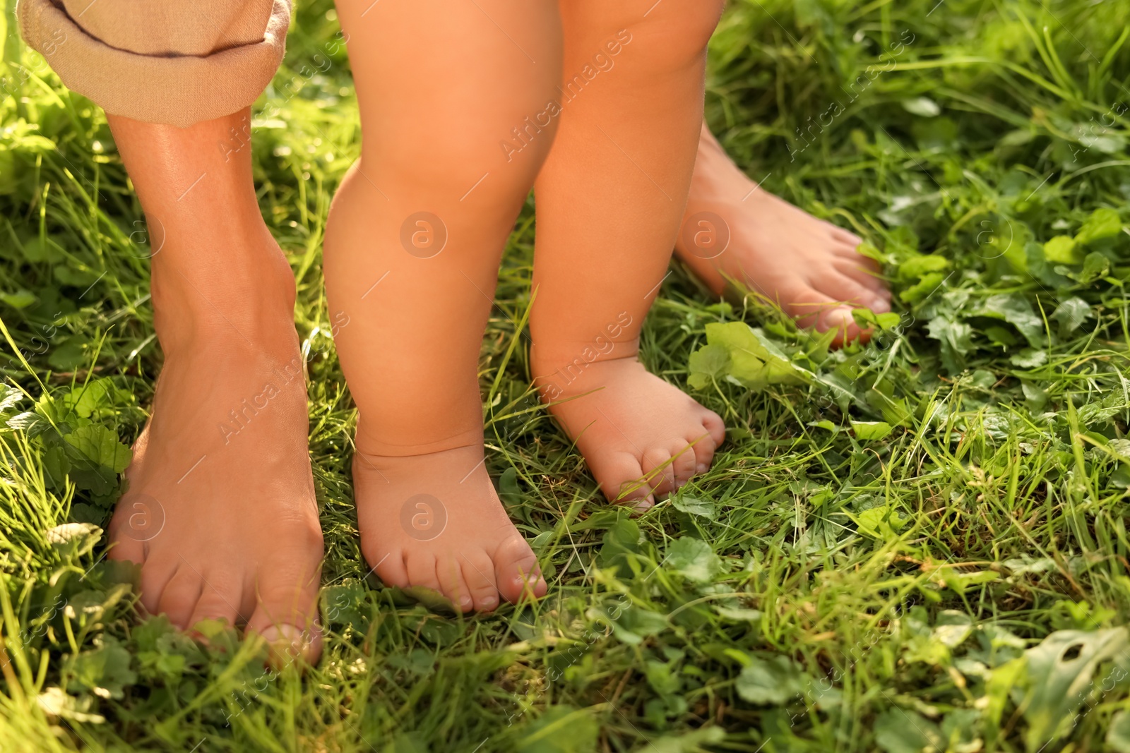 Photo of Woman with her child walking barefoot on green grass outdoors, closeup