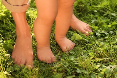 Photo of Woman with her child walking barefoot on green grass outdoors, closeup