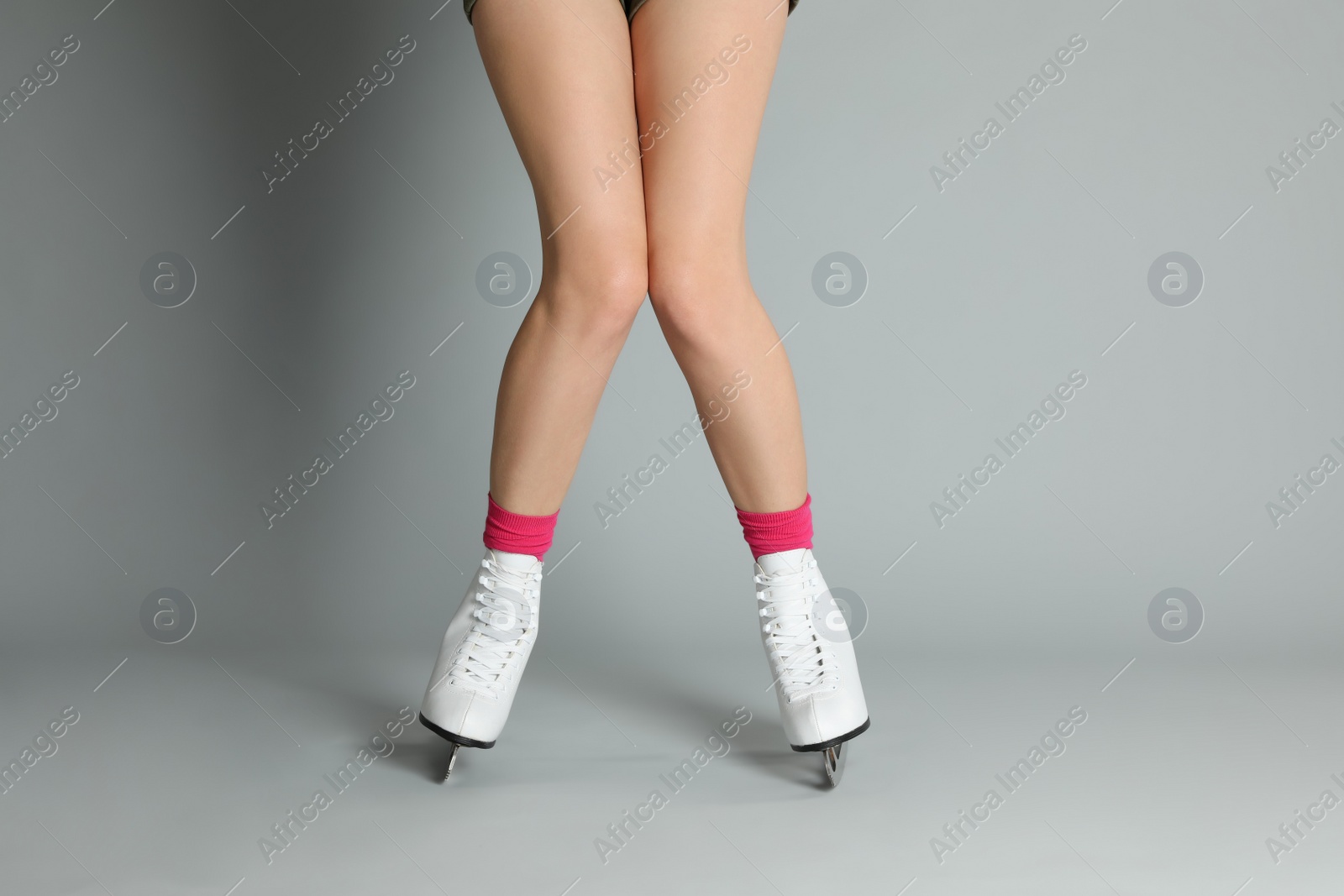 Photo of Woman in elegant white ice skates on grey background, closeup of legs