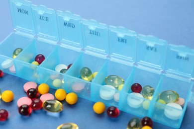Plastic box with different pills on light blue background, closeup