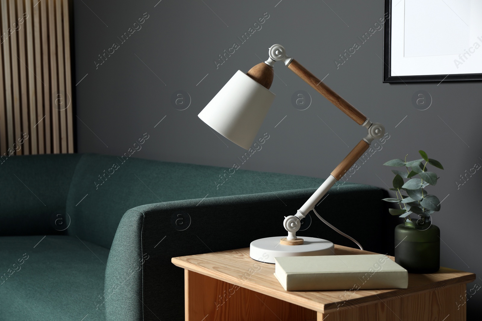 Photo of Stylish modern desk lamp, book and plant on wooden cabinet in living room