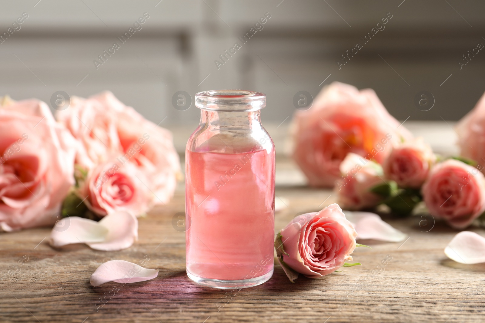 Photo of Bottle of rose essential oil and flowers on wooden table