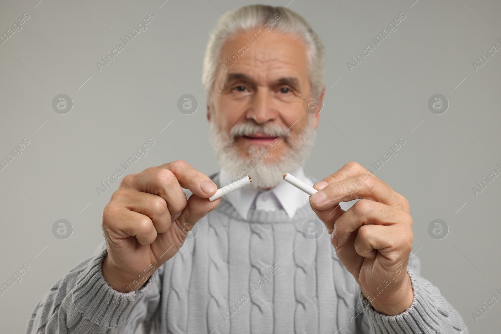 Photo of Stop smoking concept. Senior man holding pieces of broken cigarette on light grey background, selective focus