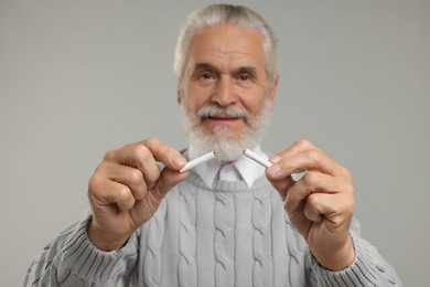 Photo of Stop smoking concept. Senior man holding pieces of broken cigarette on light grey background, selective focus