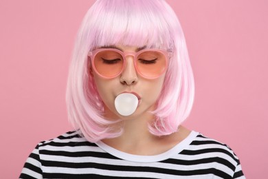 Photo of Beautiful woman in sunglasses blowing bubble gum on pink background