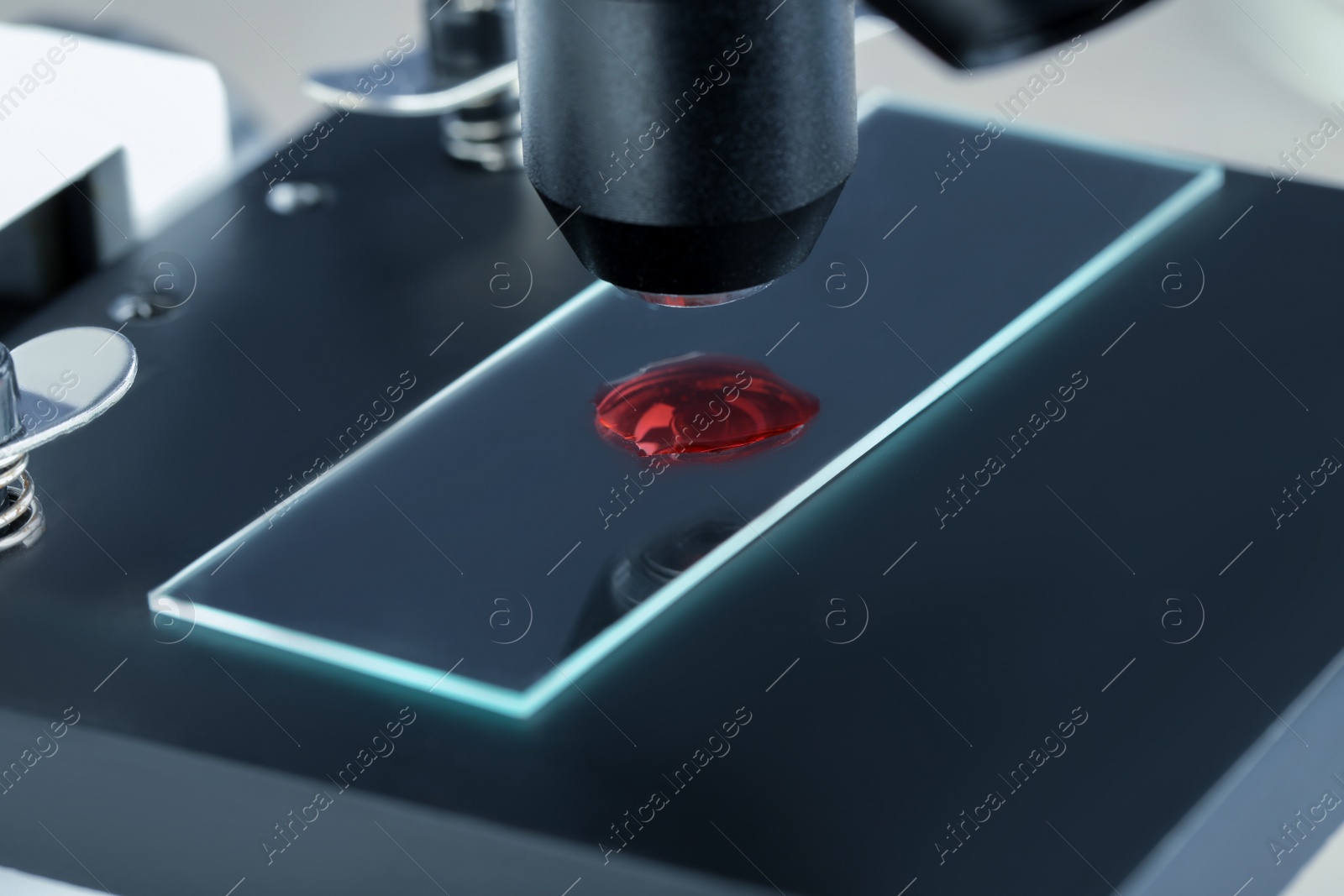 Photo of Glass slide with sample of red liquid under microscope in laboratory, closeup