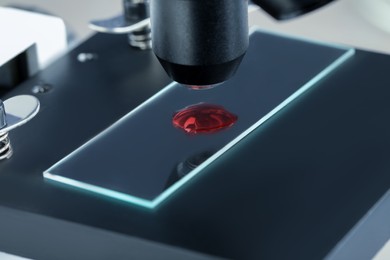Glass slide with sample of red liquid under microscope in laboratory, closeup