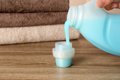 Photo of Woman pouring detergent into cap on table, closeup. Laundry day