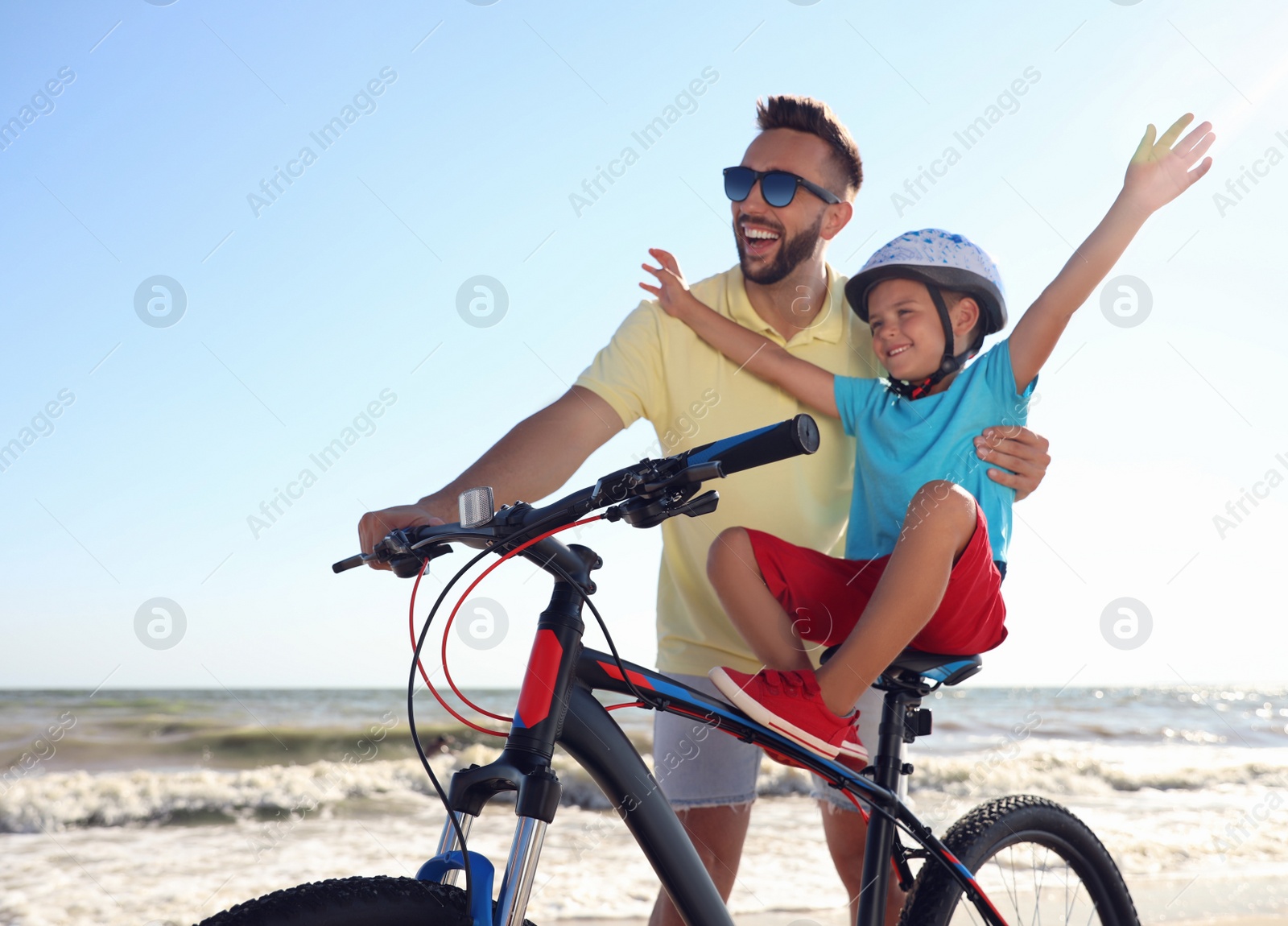 Photo of Happy father teaching son to ride bicycle on sandy beach near sea