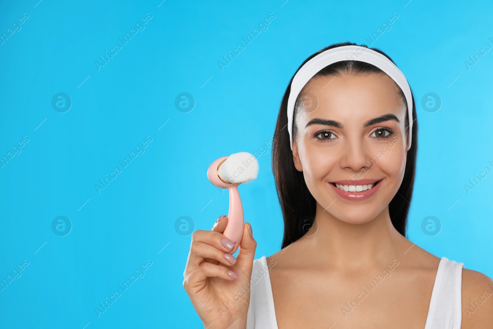 Photo of Young woman holding facial cleansing brush on light blue background, space for text. Washing accessory