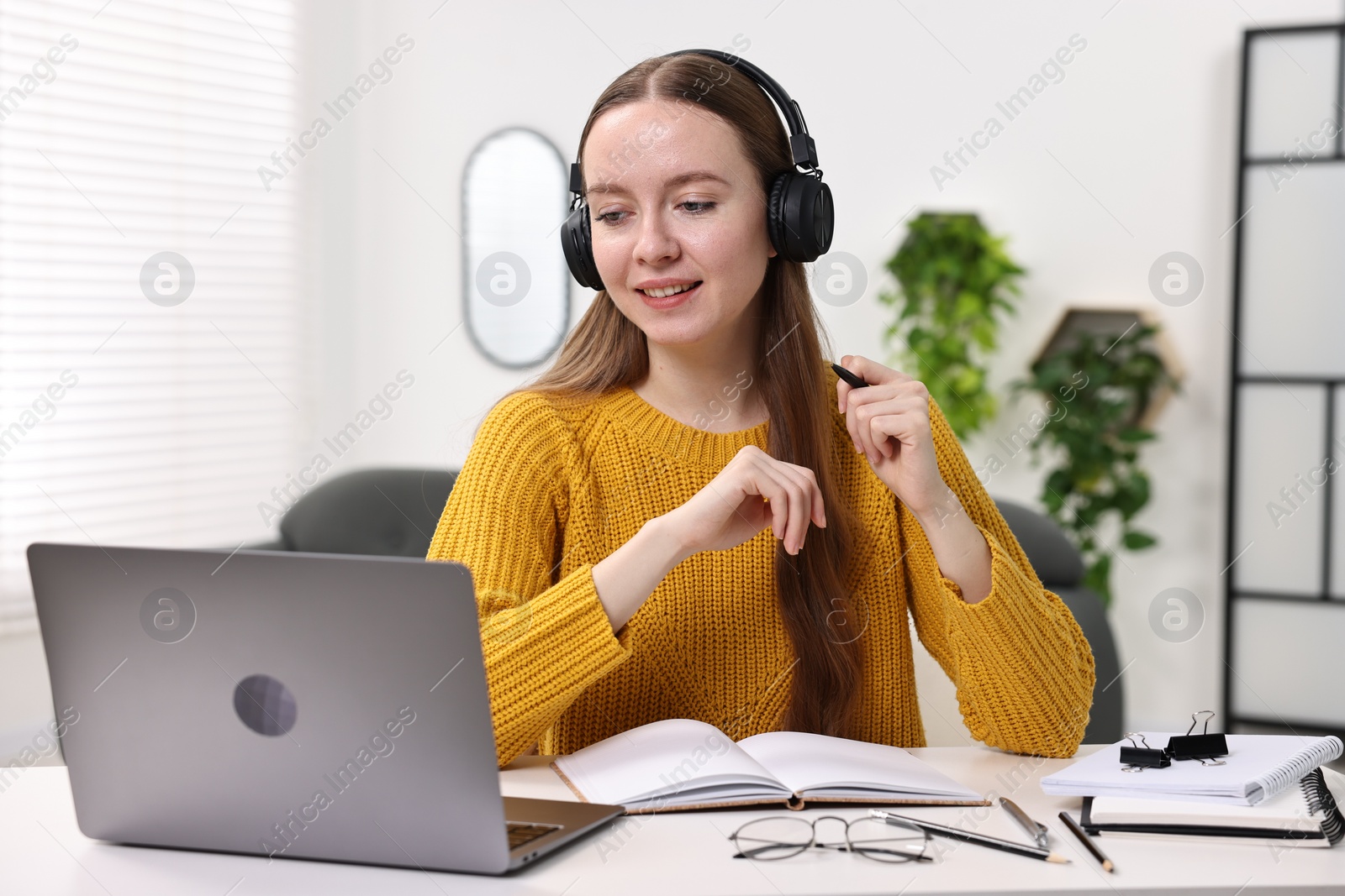 Photo of E-learning. Young woman using laptop during online lesson at white table indoors