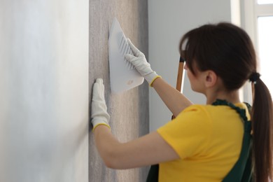 Woman smoothing stylish gray wallpaper in room