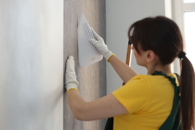 Photo of Woman smoothing stylish gray wallpaper in room