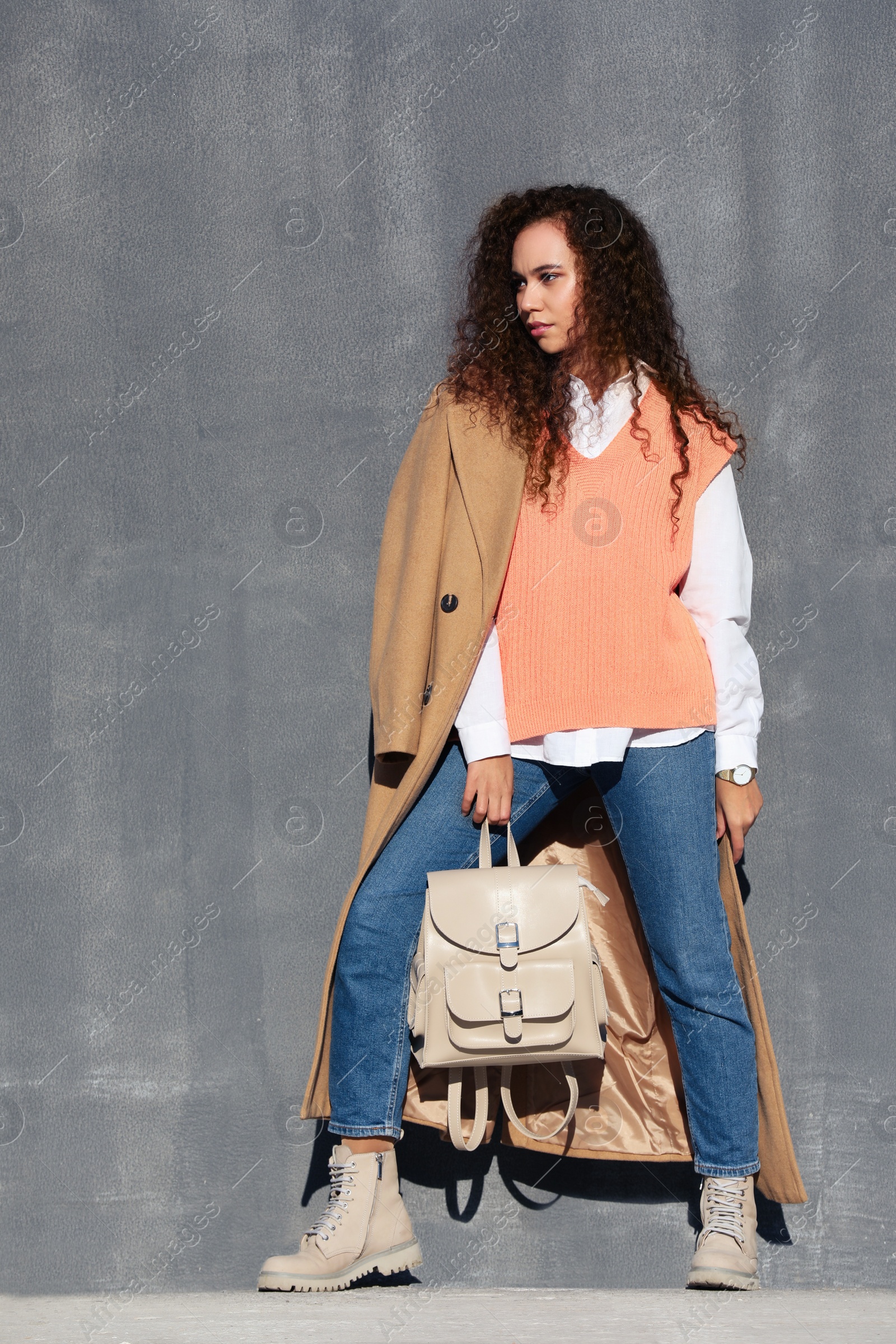 Photo of Full length portrait of beautiful African-American woman with stylish beige backpack near grey wall outdoors